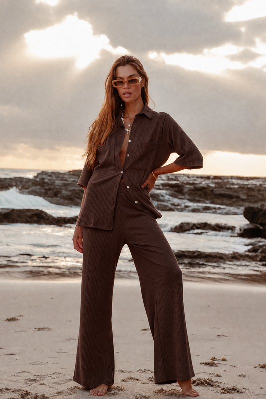 Woman in a brown outfit standing on a beach with a sunset in the background