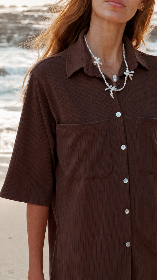 Person wearing a brown shirt with a necklace on a beach
